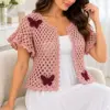 Dusty pink crochet cardigan with burgundy butterfly appliques, open lattice body, and scalloped edging worn over white dress