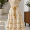 Ivory crochet shell dress with honey gold trim and scalloped skirt displayed on dress form in bright room